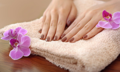 Obraz na płótnie Canvas Female hands with brown manicure and orchid flowers on towel, closeup