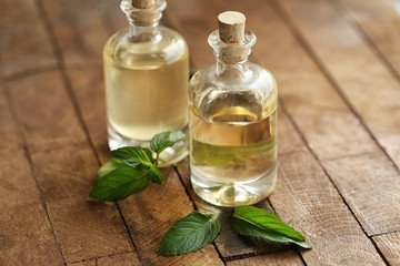 Bottles with mint oil and fresh leaves on wooden background