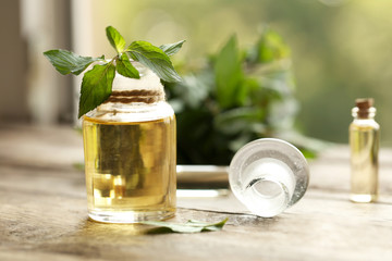 Bottle with mint oil and fresh leaves on blurred natural background