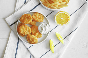 Tasty nuggets with sauce in plate and lemon on napkin