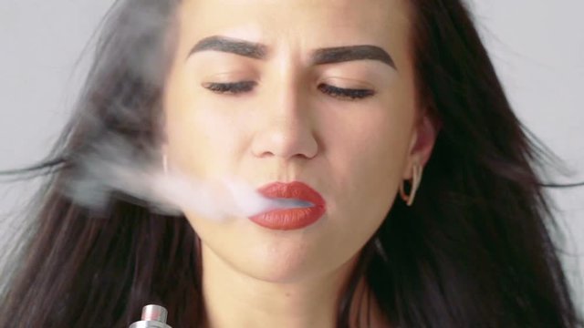 Portrait of woman blowing e-cigarette fume on beige background. Slowly