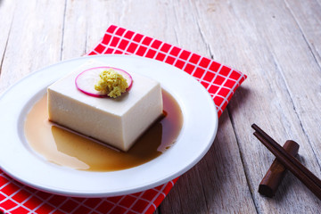 Close up of tofu on a white plate with soy sauce on a wooden tab