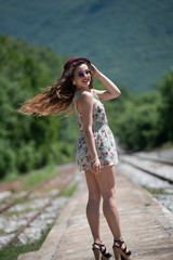 Fototapeta na wymiar Portrait of a pretty girl with curly hair wear floral dress, sunglasses and red bowler hat, walking on a old docks train station