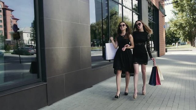 Happy young female friends walking together after shopping. Slow motion