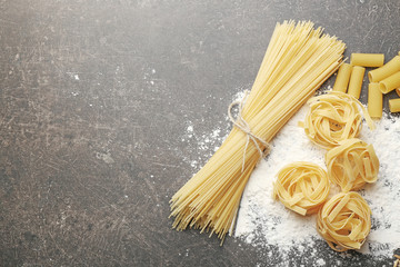 Different dry pasta with flour on grey table