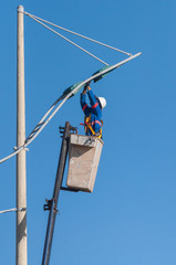 Man working replacing bulb of a lamp post. The worker is wearing safety equipment. Man swapping pole lamp with a crane.