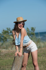 Pretty woman with long curly hair wear spaghetti strap, shorts and hat. Sea, sky and greens as background