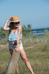 Pretty woman with long curly hair wear spaghetti strap, shorts and hat. Sea, sky and greens as background