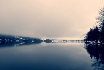 Winter landscape on the lake in black and white, with trees reflecting on still water surface. Monochrome image filtered in nostalgic, vintage style with soft focus and red filter; high contrast. - 121774374