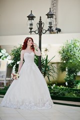 Portrait of charming red-haired bride model with wedding bouquet at hand posed background lantern on great wedding hall indoor