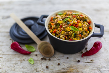 Millet groats with ground beef and vegetables and herbs in a pot on a wooden table