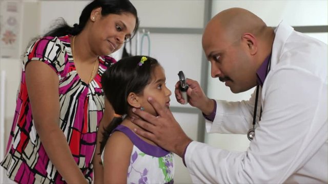 A pediatrician or family doctor gives a wellness checkup to a little patient who is being reassured by her mother.