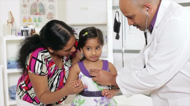 A pediatrician or family doctor gives a wellness checkup to a little patient who is being reassured by her mother.