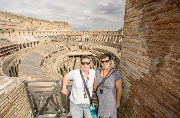 Two women tourists smile happily and pose as they do an audio tour of the Coliseum in Rome.