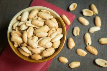 Roasted peeled salted peanuts in rustic bowl on wooden background (focus on peanut in bowl)