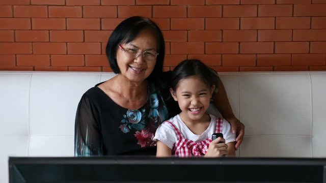 4K : Asian senior woman with little girl watching TV on sofa together, Tilt down shot