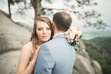 Gorgeous bride, groom kissing and hugging near the cliffs with stunning views