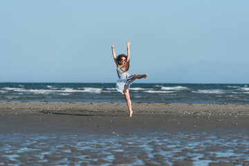 Woman with long curly hair wear dance dress and making moves, standing on the beach. Wind wave the skirt. Sea and sky as background