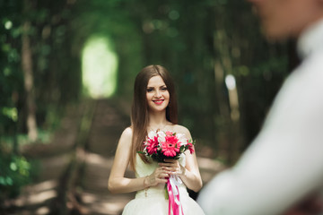 Bride posing and smiles while groom waits on the background