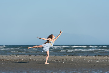 Fototapeta na wymiar Woman with long curly hair wear dance dress and making moves, standing on the beach. Wind wave the skirt. Sea and sky as background