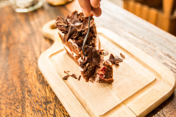 Woman hand use frok to cutting the Slice of chocolate cake with cherries topping on wood table.