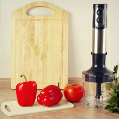 Red bellpepper with tomato and a blender on the kitchen table, gently toned