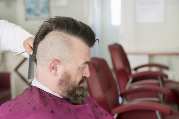 Barber makes a mohawk hairstyle of a adult bearded man