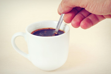 Hand mixing with a spoon of aromatic coffee in the cup, gently toned