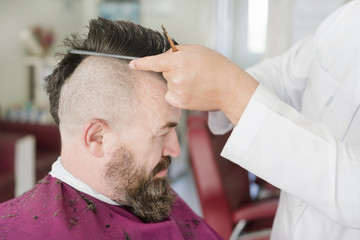 Barber makes a mohawk hairstyle of a adult bearded man