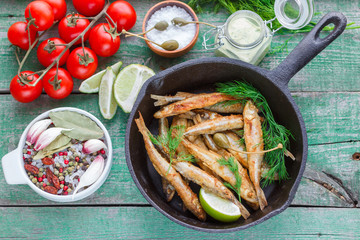 Fried small fish. Fried smelt in the pan on the table with a sauce, lime, tomatoes, dill and garlic. A traditional Russian dish
