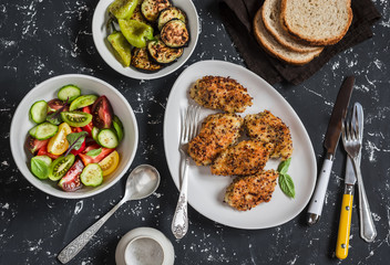 Quinoa crusted chicken, vegetable salad, grilled eggplant and pepper - dinner table. On a dark background, top view