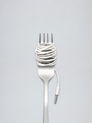 Food for new generation / A shining fork with noodle made of cable with music jack plug in metal background.
