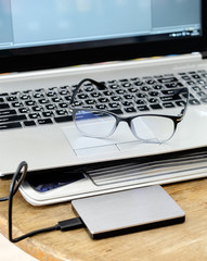 Notebook grey modern black keyboard with hdd grey and spectacles on wooden table