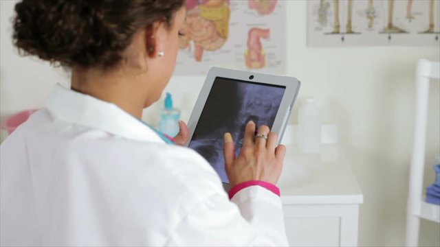 A doctor in a clinical setting views an x-ray on an electronic tablet she is using.