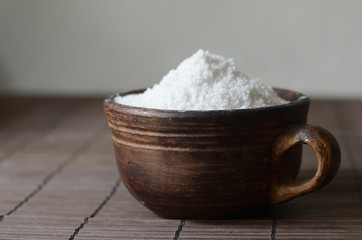 Salt in a brown ceramic bow on a wooden tablel. Rustic still life