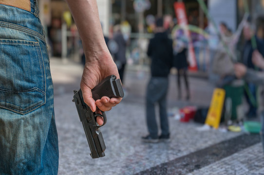Gun control concept. Armed man - attacker holds pistol in hand in public place. Many people on street.