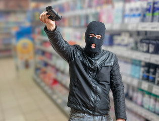 Robbery in store. Robber is threatening and aiming with pistol in shop.