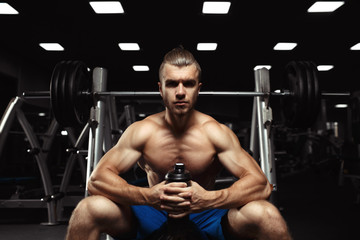 Fototapeta na wymiar Young muscular man sitting with a bottle of water in the gym