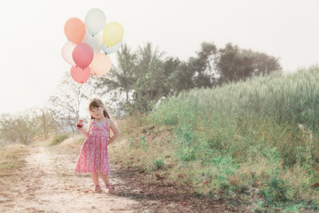 Little asian girl playing with balloons on wheat field