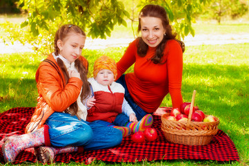 Family with mother and children in the park in autumn with a basket of apples