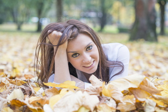 Portrait of smiling young woman lying on autumn leaves.