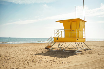 Footprints and wheeltracks on the sand beyond an empty yellow lifeguard cabin on a deserted beach