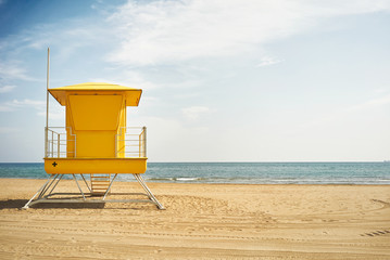 Quiet blue sky and sea and a saturated yellow lifeguard post on a deserted beach in beautiful weather