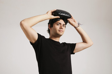 A young man in unlabeled black t-shirt putting on VR headset looking into the camera isolated on white