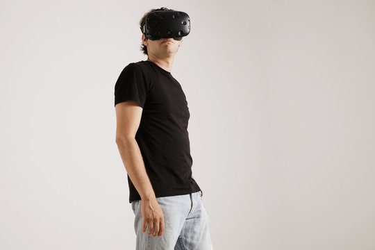 Low angle shot of a man wearing VR headset, blank black t-whirt and jeans looking around isolated on white