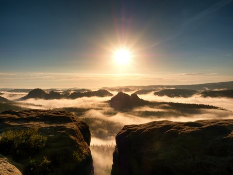 Fototapeta bright orange daybreak. Sandstone cliff above deep misty valley in Saxony Switzerland. Hilly peaks sticking out from creamy fog.