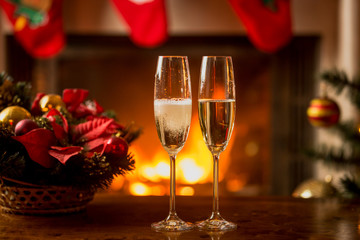 Closeup of two glasses of champagne in front of burning fireplac