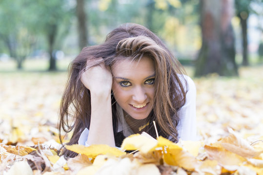 Portrait of young woman lying on autumn leaves.