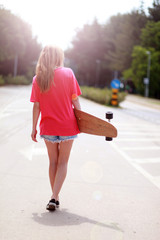 Surfer Girl läuft mit Longboard Richtung Sonne