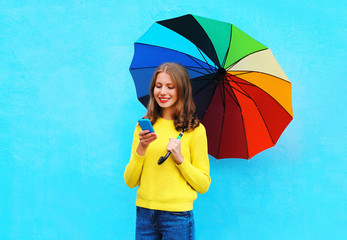 Happy pretty smiling young woman with colorful umbrella using sm